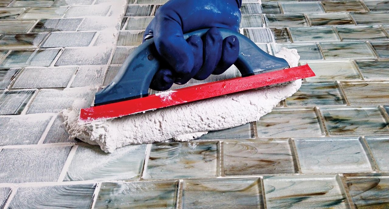 Person wearing rubber gloves using Prism SCG and a float to grout verigated blue glass tile.