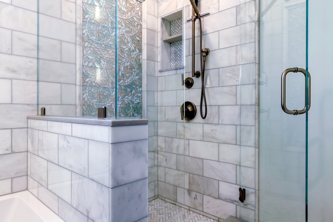 Colorful mosaic tile work in white tiled shower with glass door.