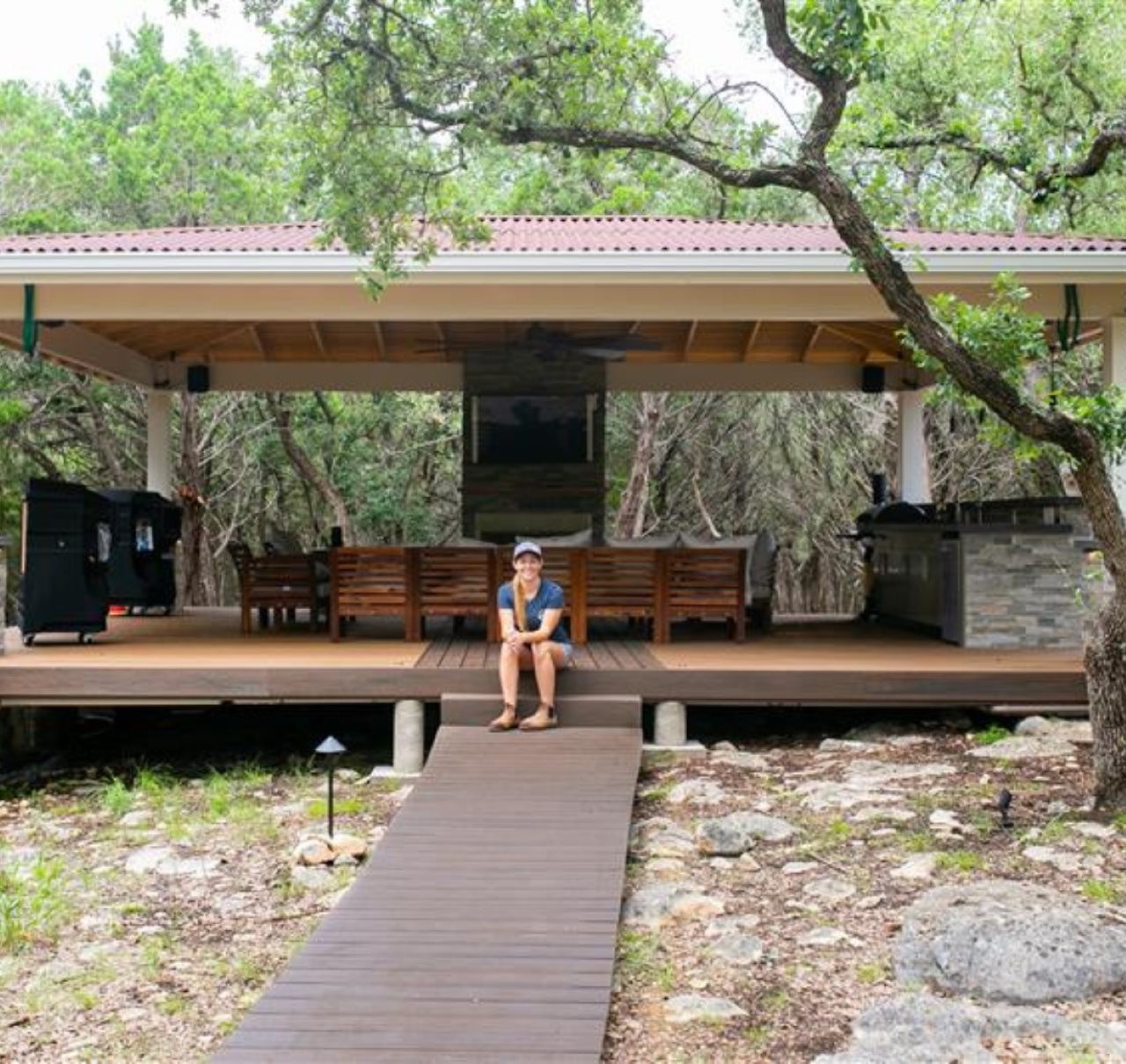 Woman sitting on a beautiful deck with out door kitchen and seating area.