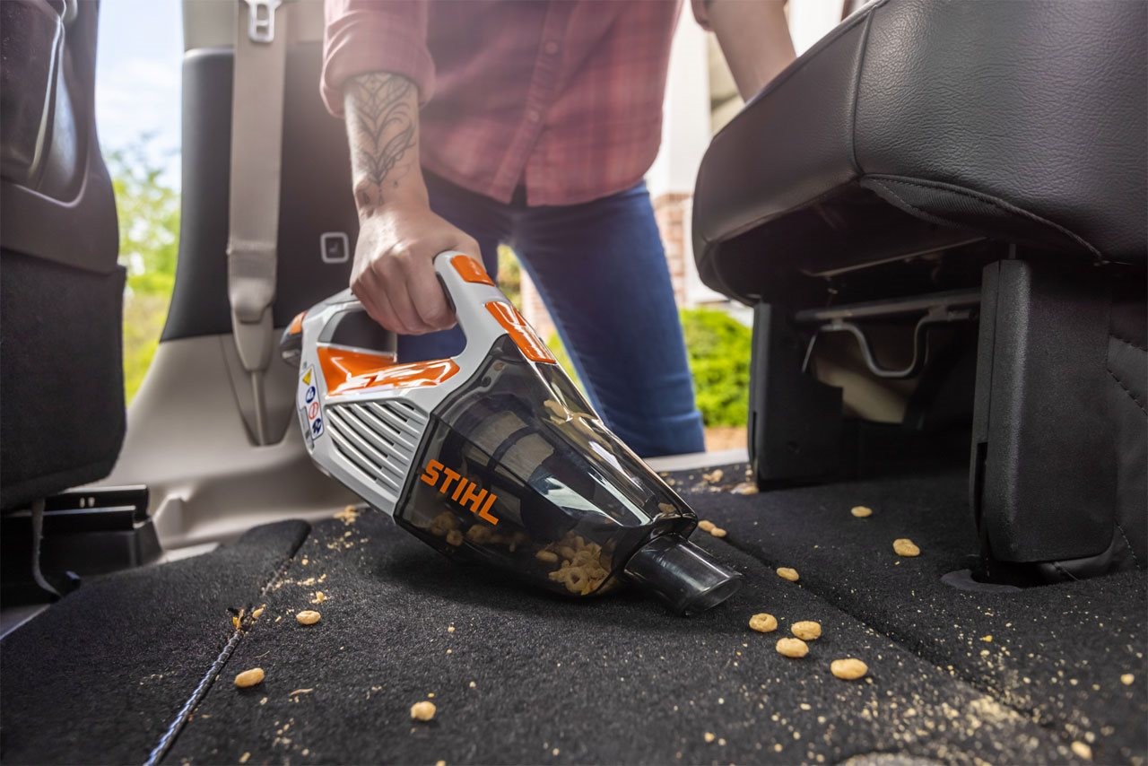 Person wearing plaid shirt using the STIHL SEA 20 vaccuum to cleanup a child's cereal snack off the floor in the back seat of a mini van.