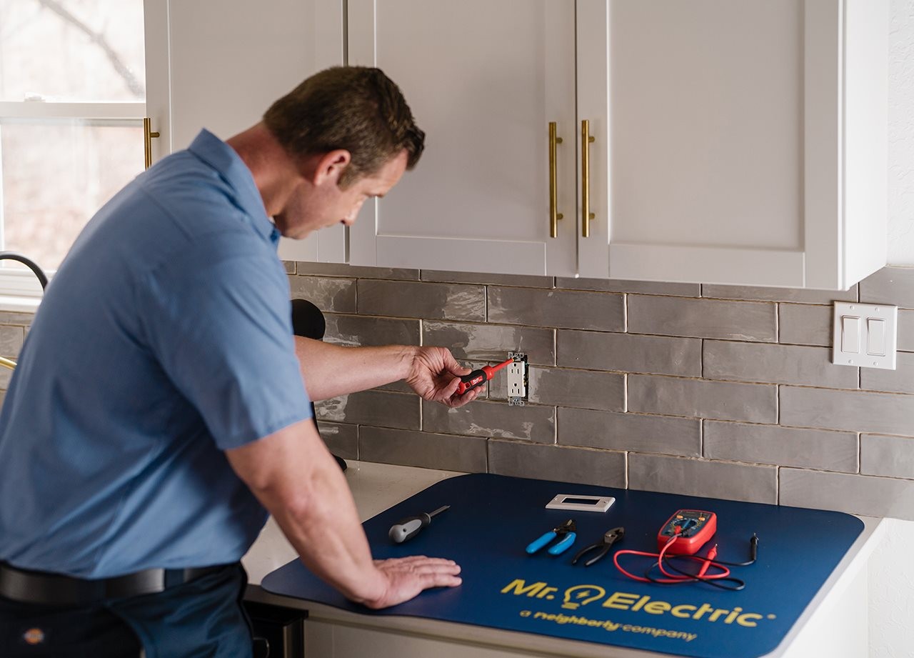 Representative from Mr. Electric working on a electrical box in the kitchen on the back splash near the sink
