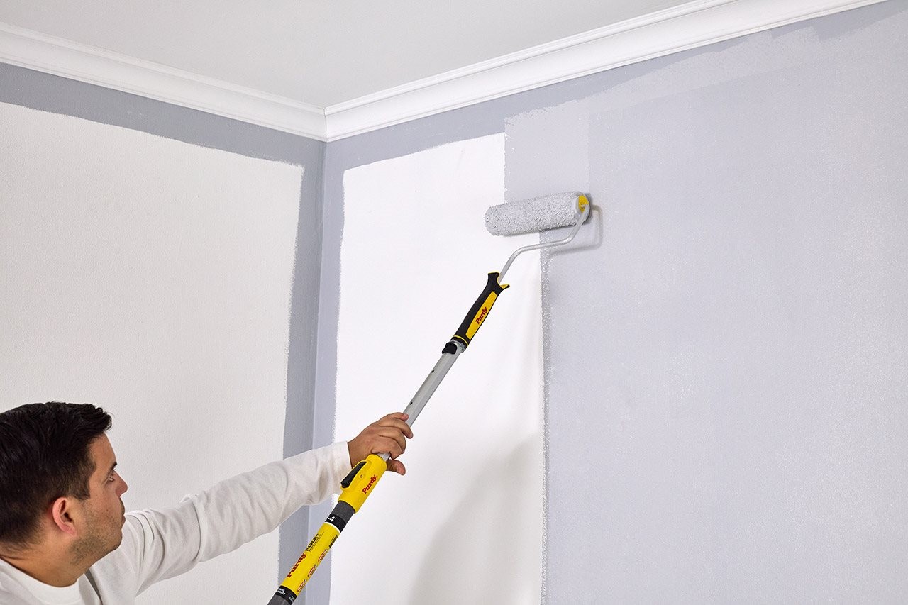 Man using an extension Purdy POLE+ and a roller to paint at wall in the livingroom.