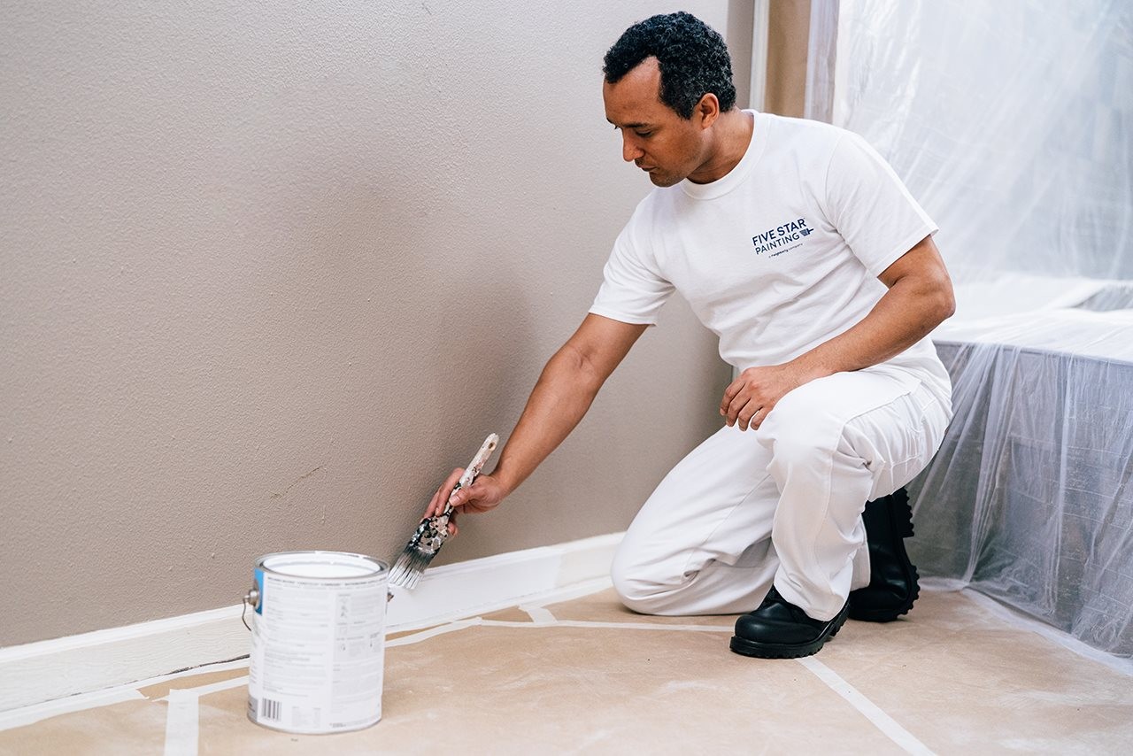 Representative from Five Star Painting making improvements in a livingroom by painting the trim with a fresh coat of paint.