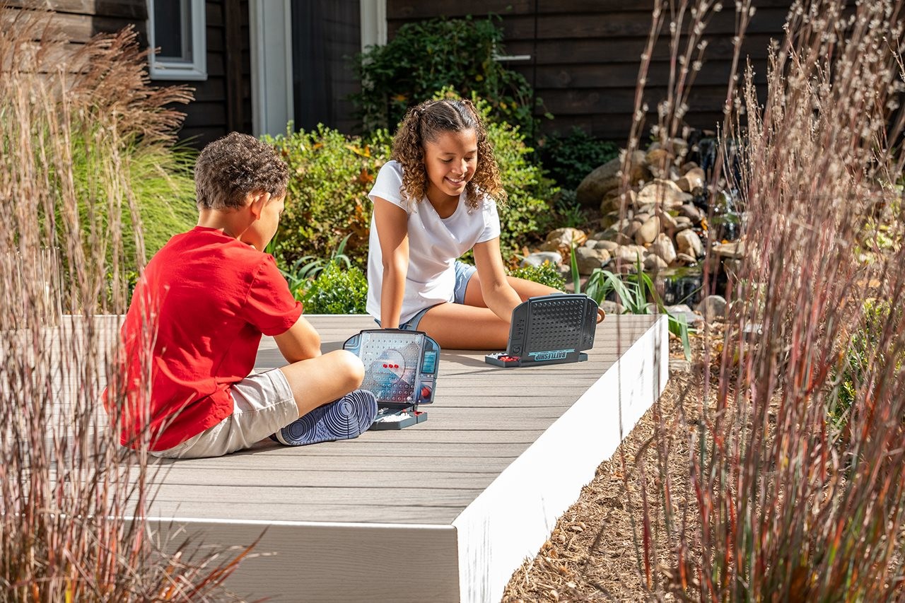 Two kids sitting on a Trex deck enjoying the sunshine while playing a game together.