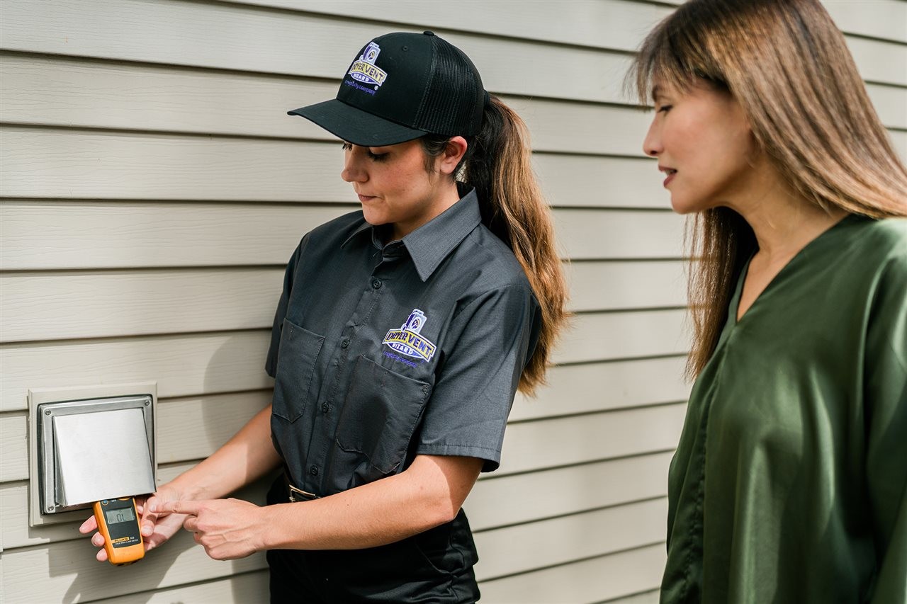 Dryer vent wizard representative showing her customer the air flow rating outside the home at the dryer vent.