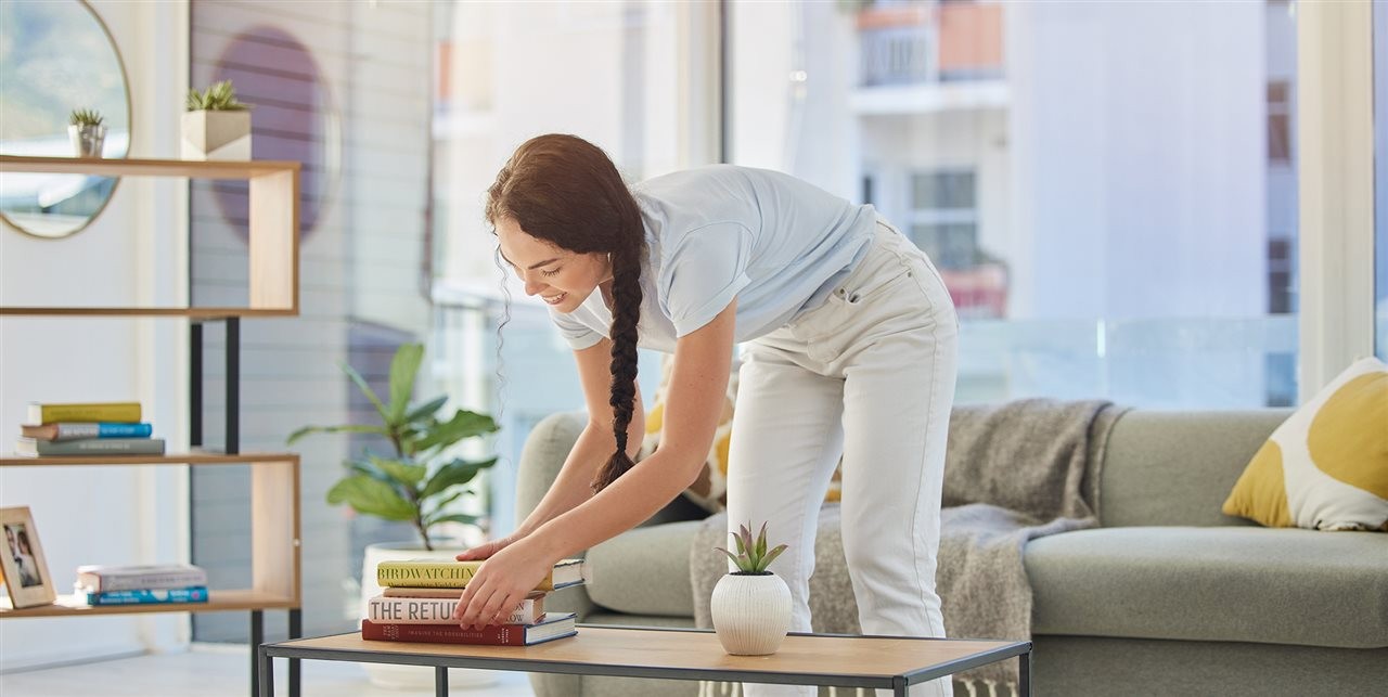 Woman moving a stack of books on a coffee table.