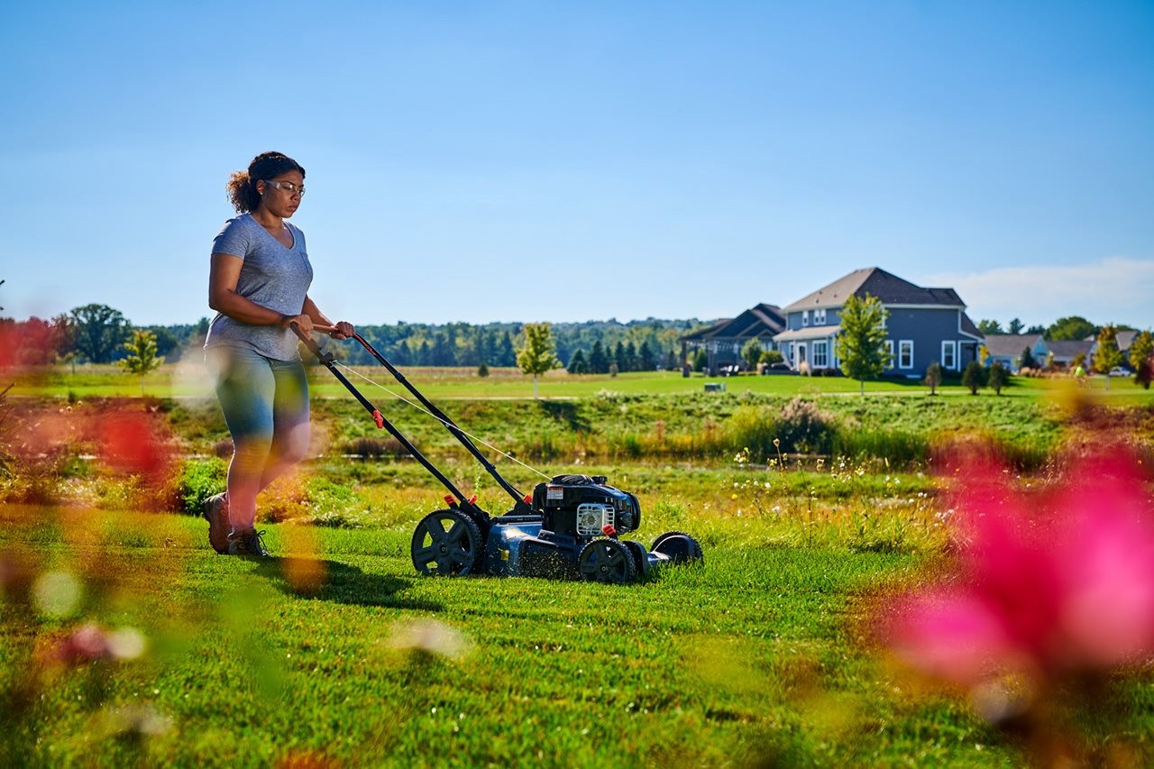 Woman pushing a gas-powered lawn mower in the backyard. Briggs and Straton builds a durable, long-running engine.